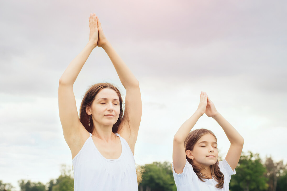 woman and daughter practicing yoga outdoors.