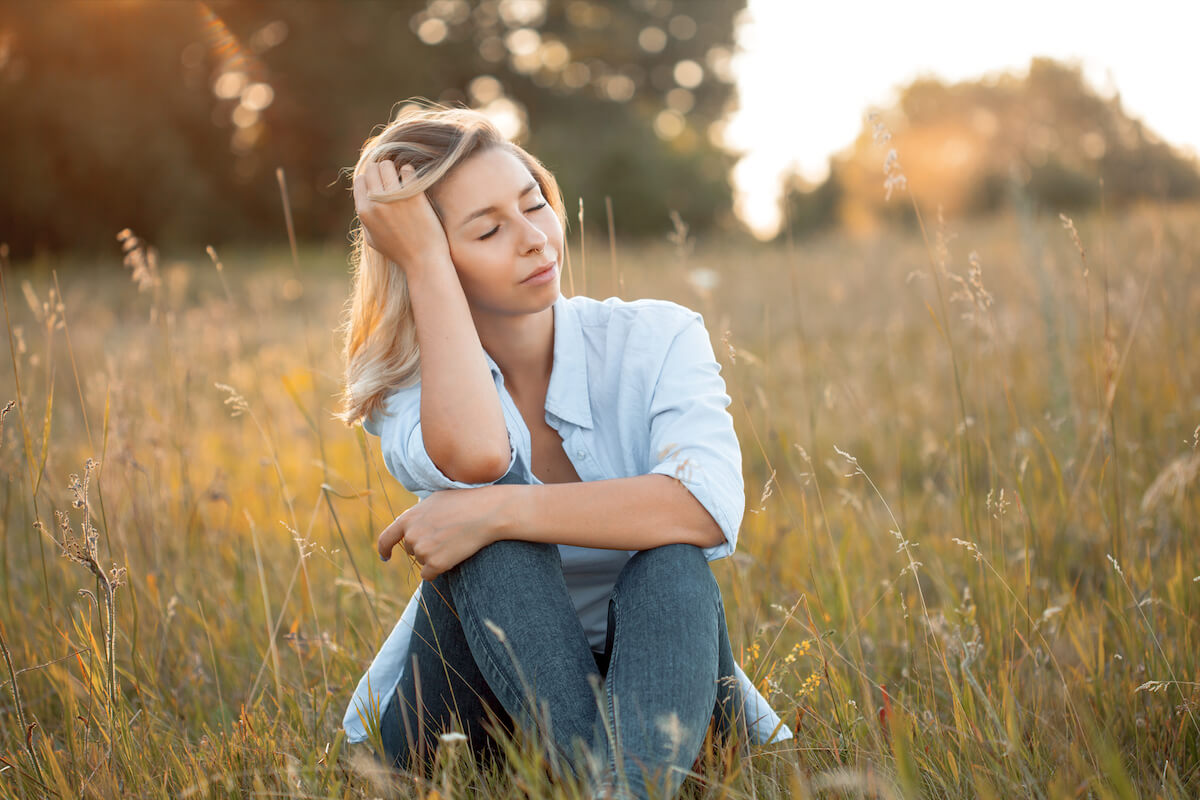 woman spending time alone in nature sitting in grass with eyes closed.