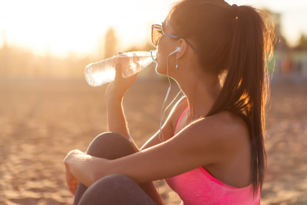 woman sitting on beach in fitness gear drinking water.