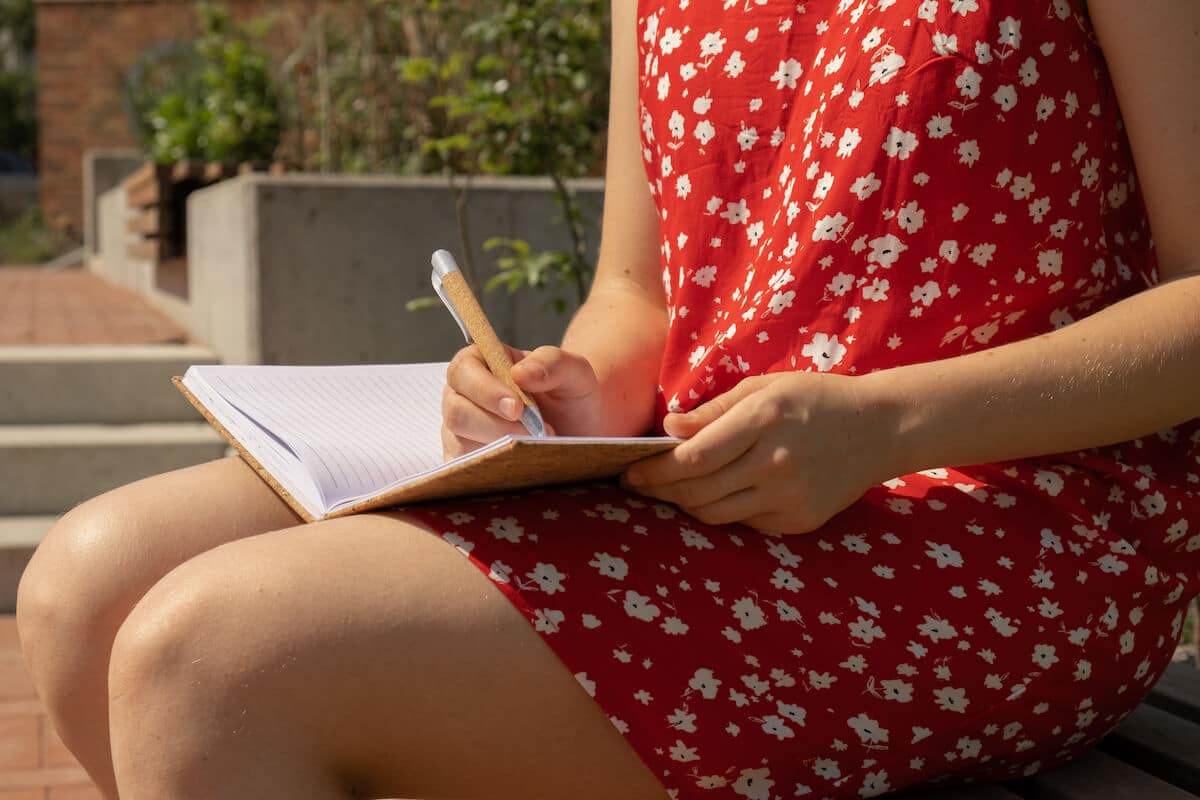 Woman in red dress writing in her journal outdoors.