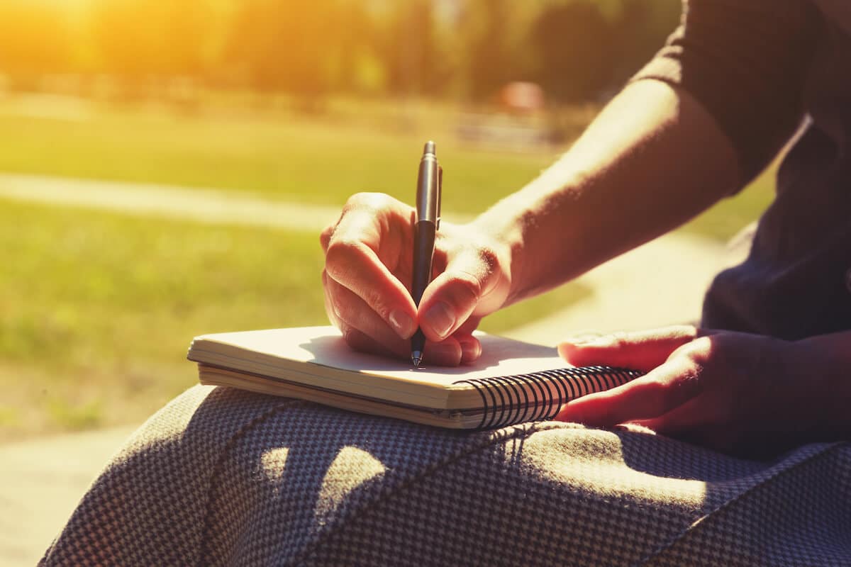 woman sitting in afternoon sun writing in a journal.