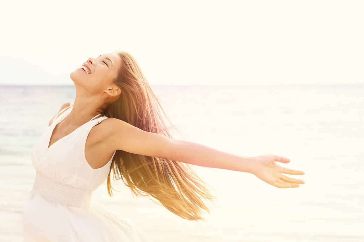 happy woman holding her arms out and feeling the fresh air on her skin while at the beach.