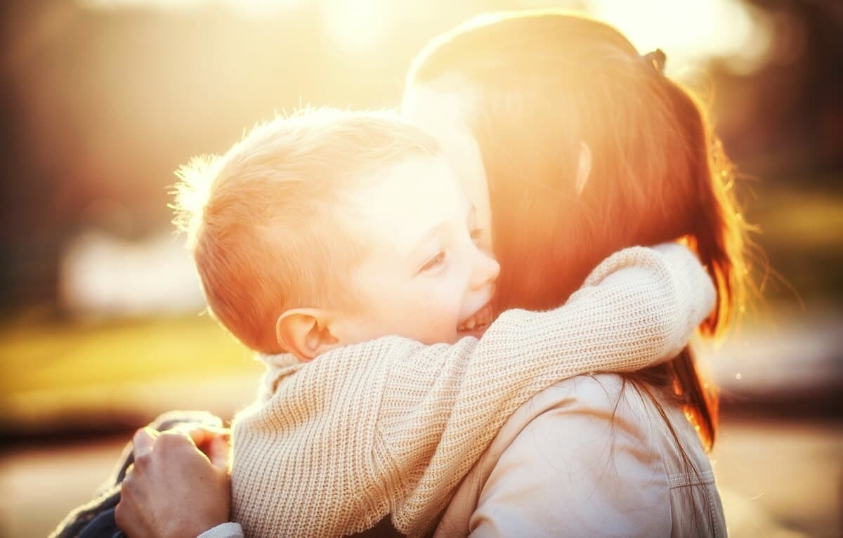 woman hugging her son outdoors as the sun lowers behind them.