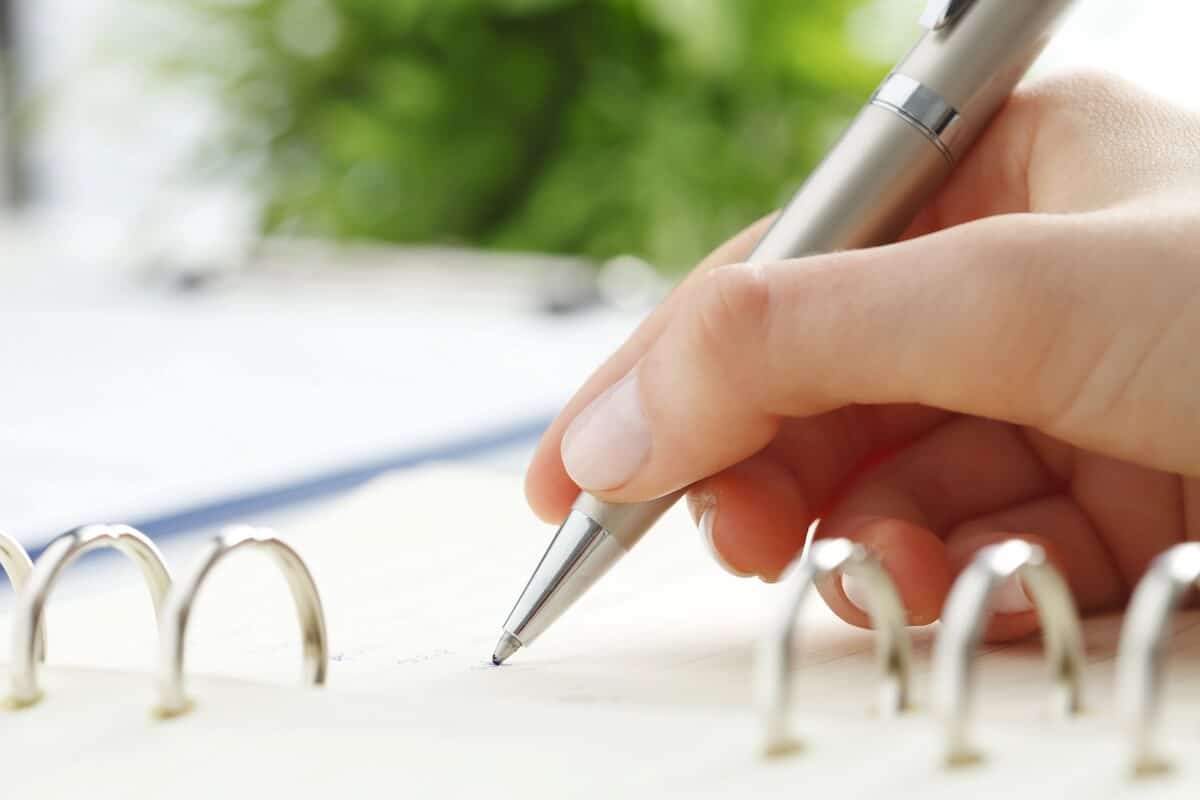 a woman's hand writing a list in a notebook with a silver pen.