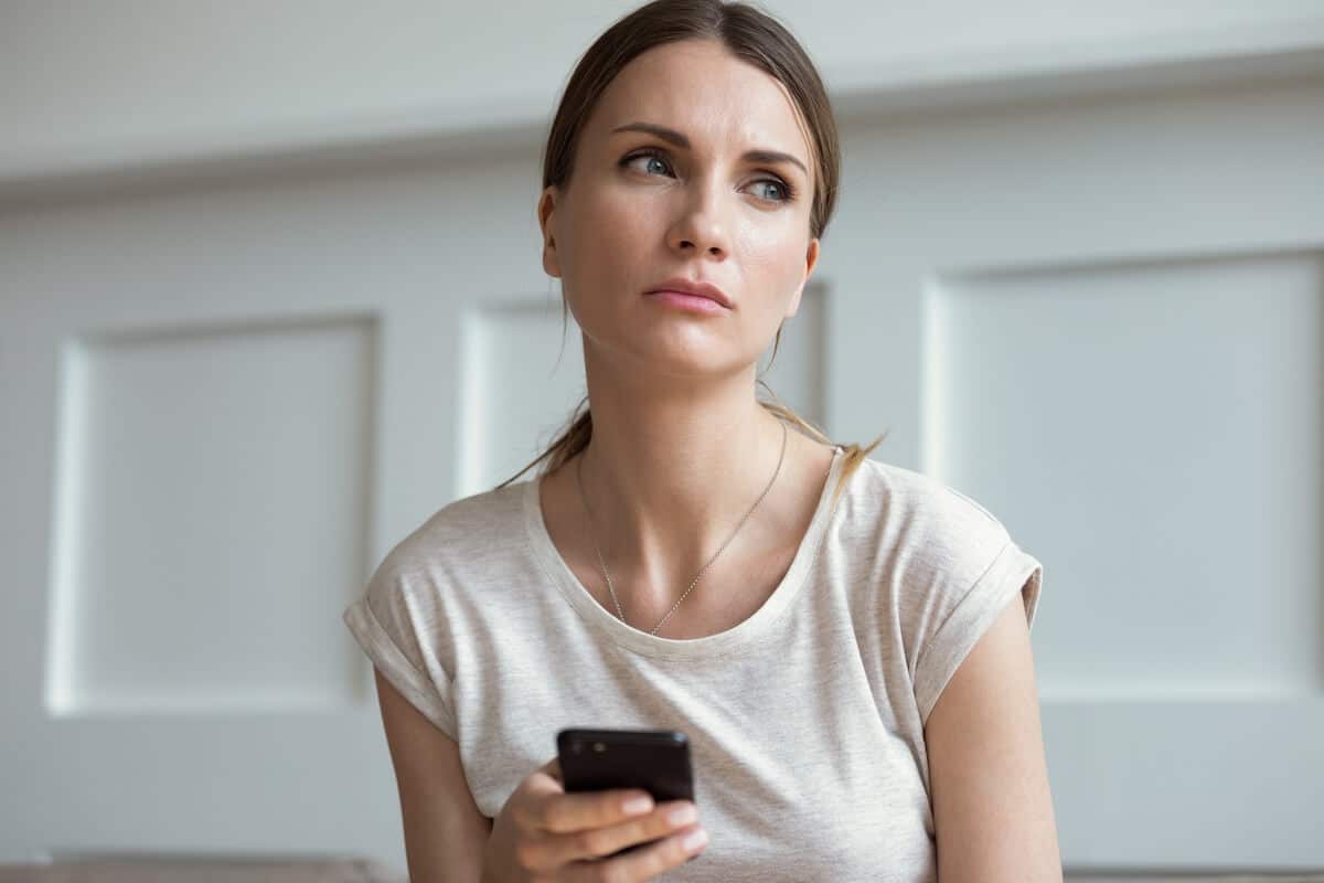 sad woman in white shirt holding a phone.