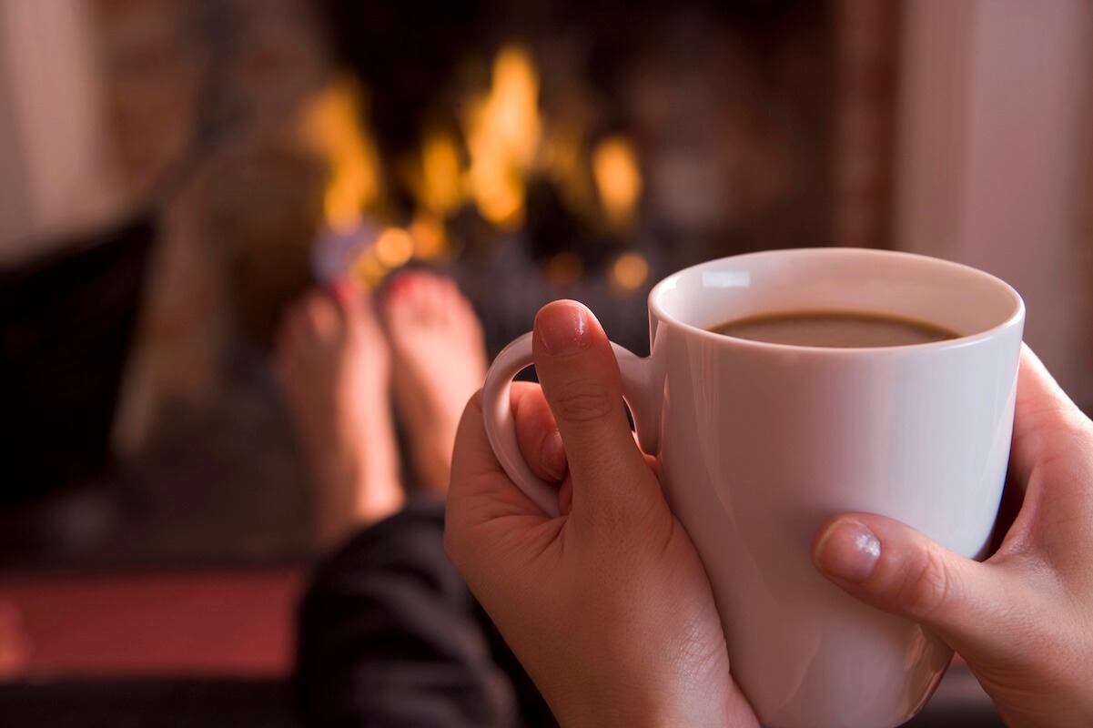woman holding a mug with fireplace in background.