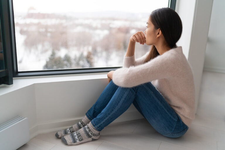 sad woman looking out window at winter scape.