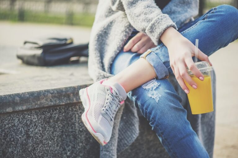 woman sitting on wall with smoothie in hand.