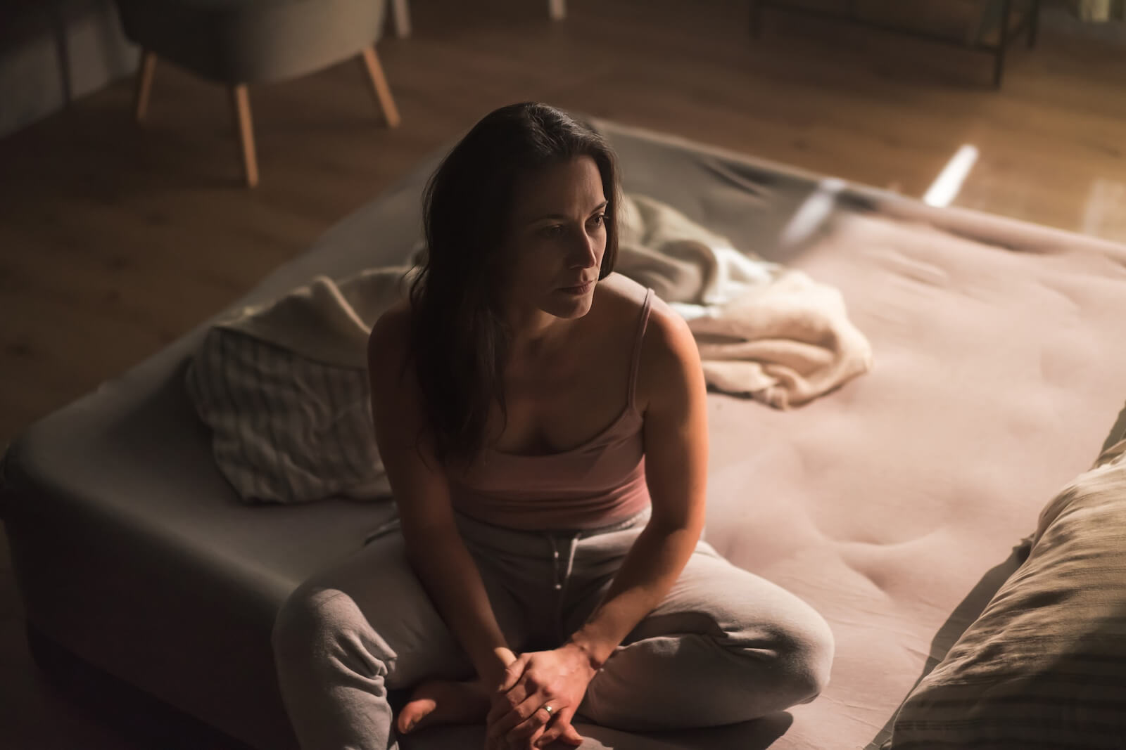 woman sitting on side of bed in the dark contemplating her day.