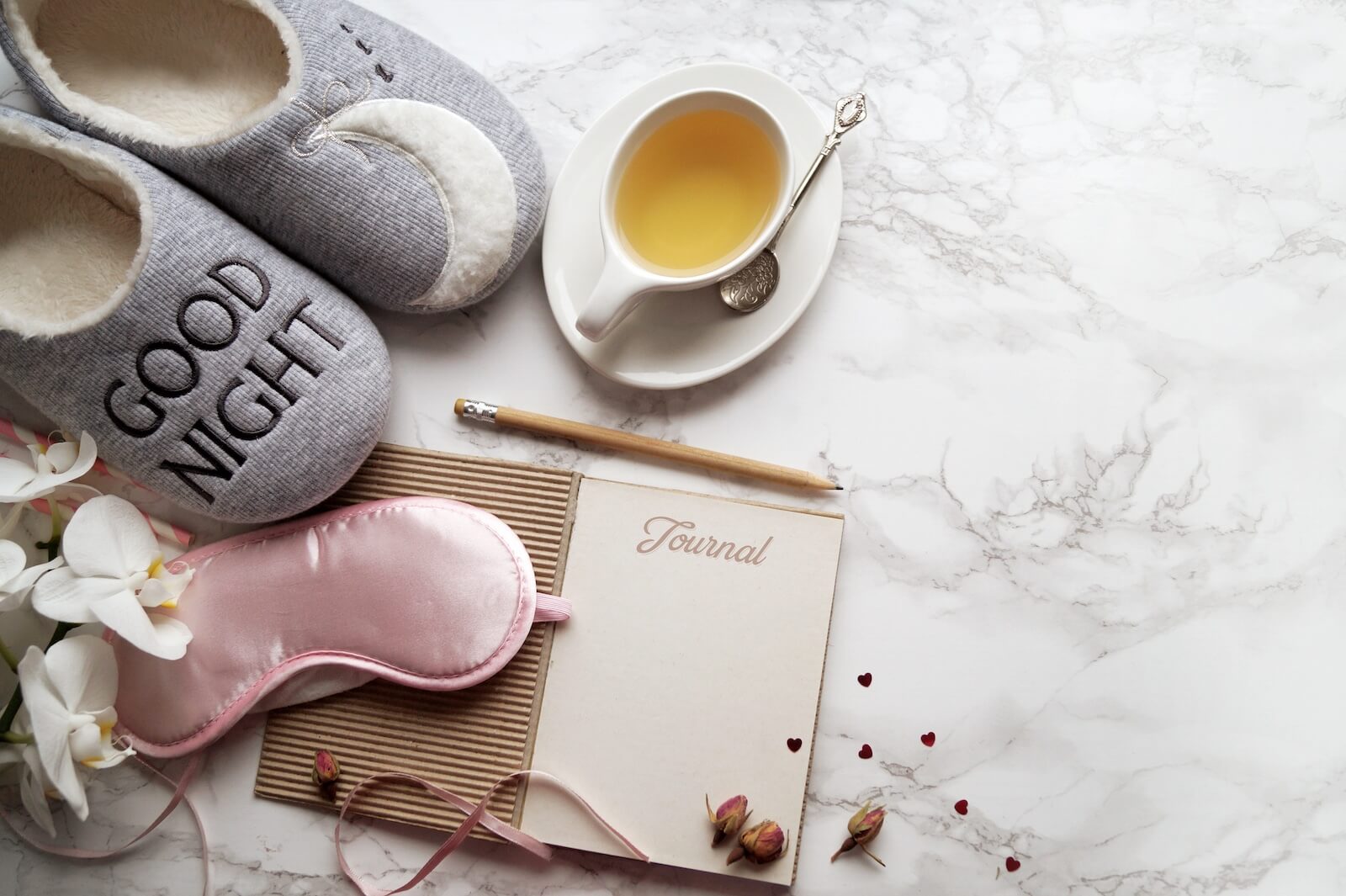 items for a nighttime self-care routine including slippers, journal, herbal tea and a sleeping mask.