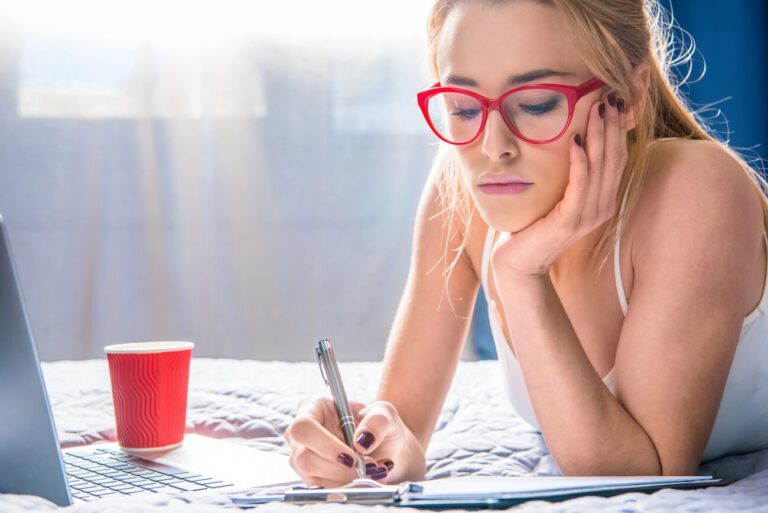 woman with red glasses writing in journal while looking stressed.