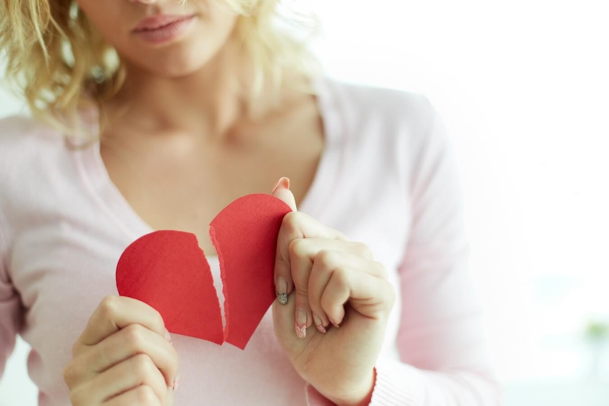 woman holding red paper heart torn in half.